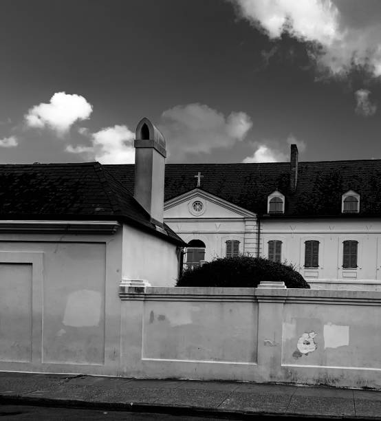 Historic building with a cross on the roof, behind a tall, weathered wall. Cloudy sky overhead, evoking a calm, timeless mood.