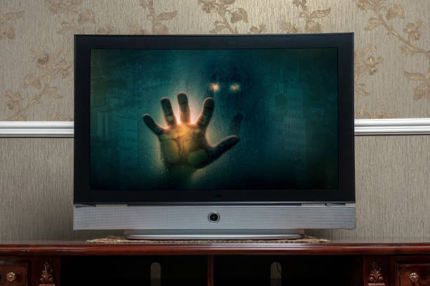 A computer screen on a table with the image of a huma hand reaching out from the screen