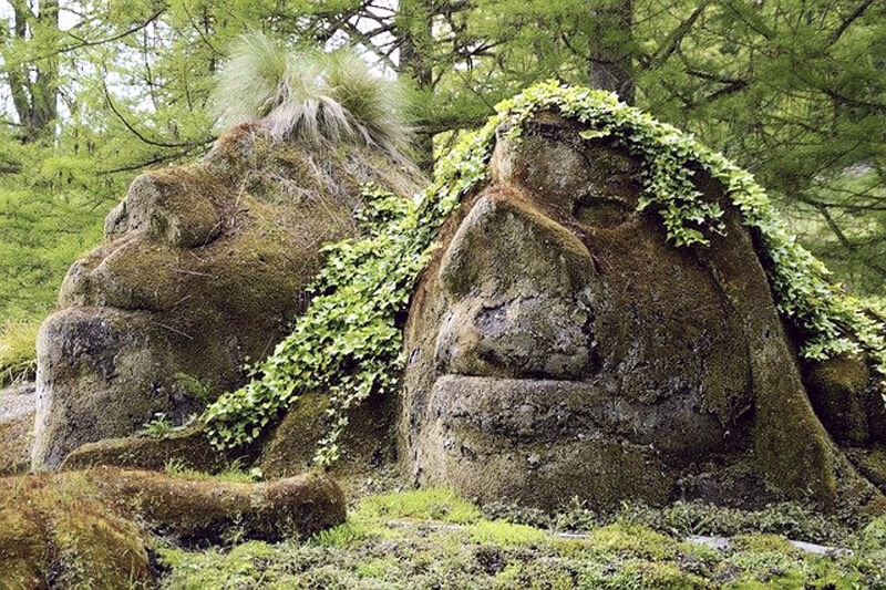 Two large boulders in a forest that resemble human heads
