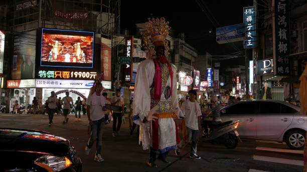 A busy Asian street at night and a Person dressed in an elaborate ghost costume is guided through the streets