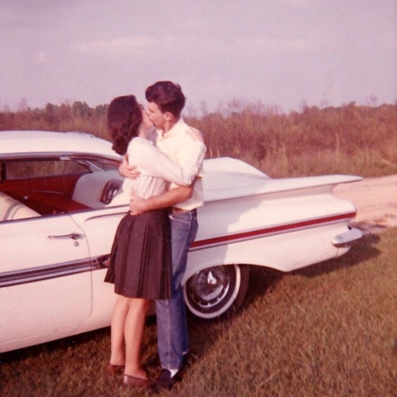 Two teenagers kissing next to a car in a field