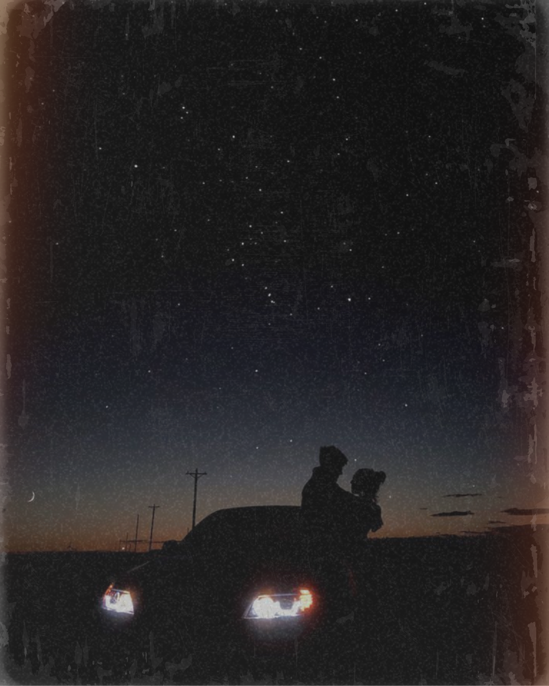 a car parked at night with the headlights on and a couple hugging next to the car