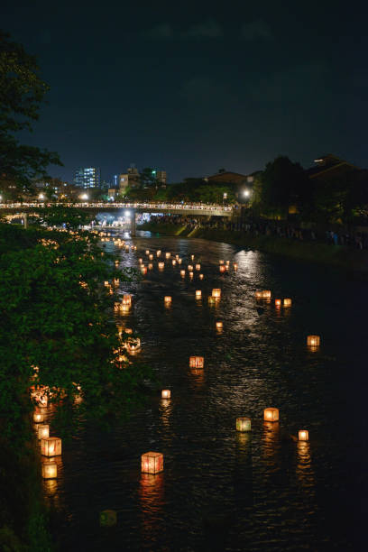 A large city at night with glowing lanterns floating down the river