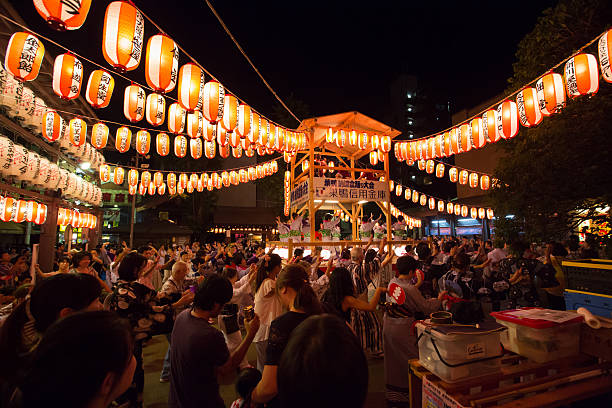 A festive street in Japan with lanterns across the sky and a crowd of people dancing
