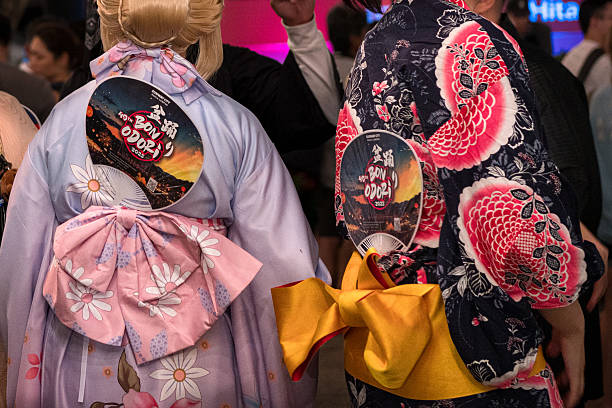 A crowded street and a close up of two kimono clad people with fans in their obi that read Bon Odori