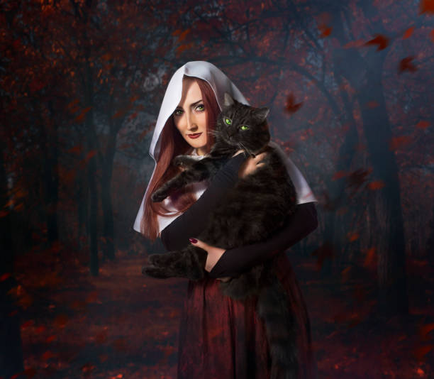 A woman in read and black in the forest holding a black cat
